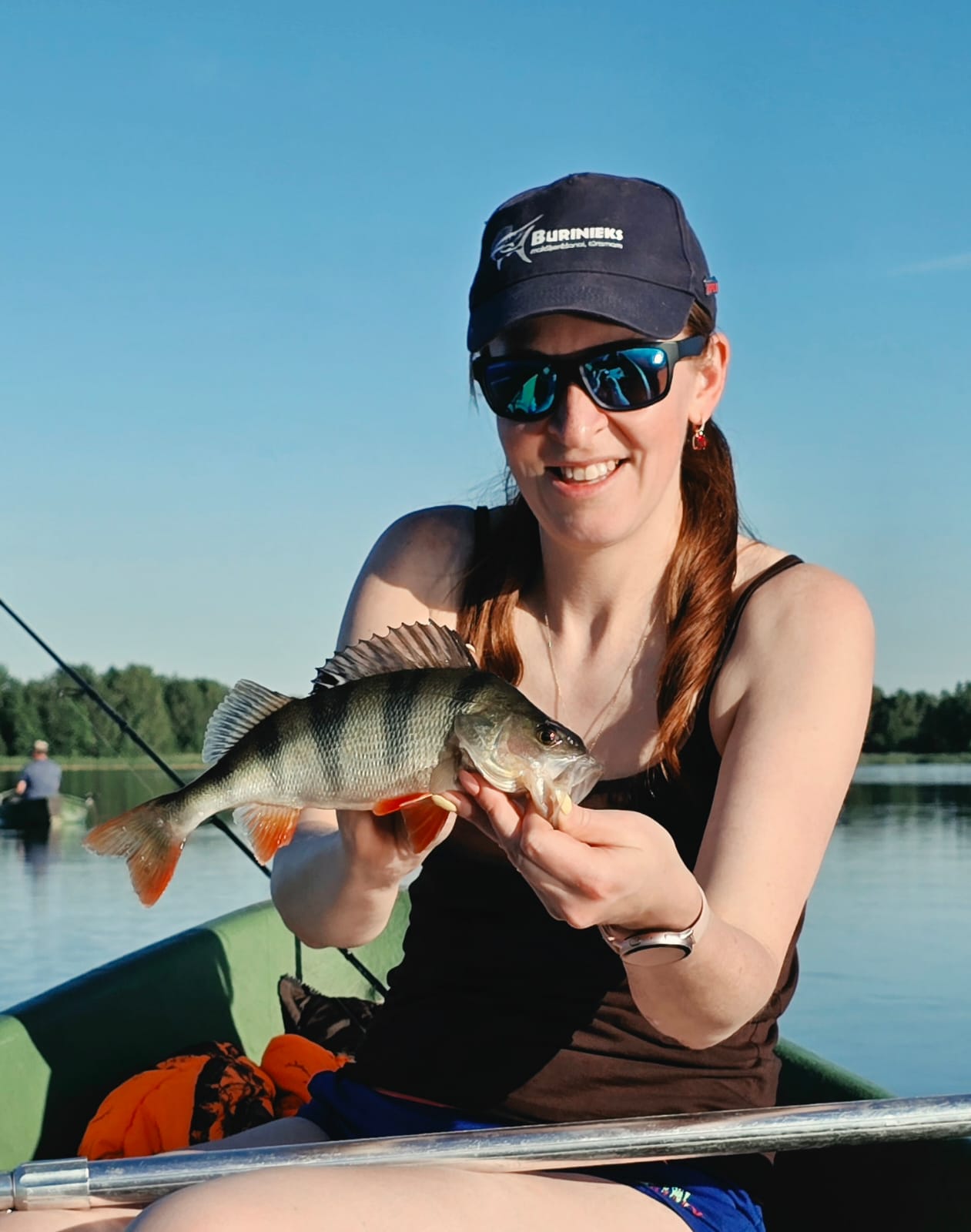 Elīna holding a perch on a boat with calm blue water behind